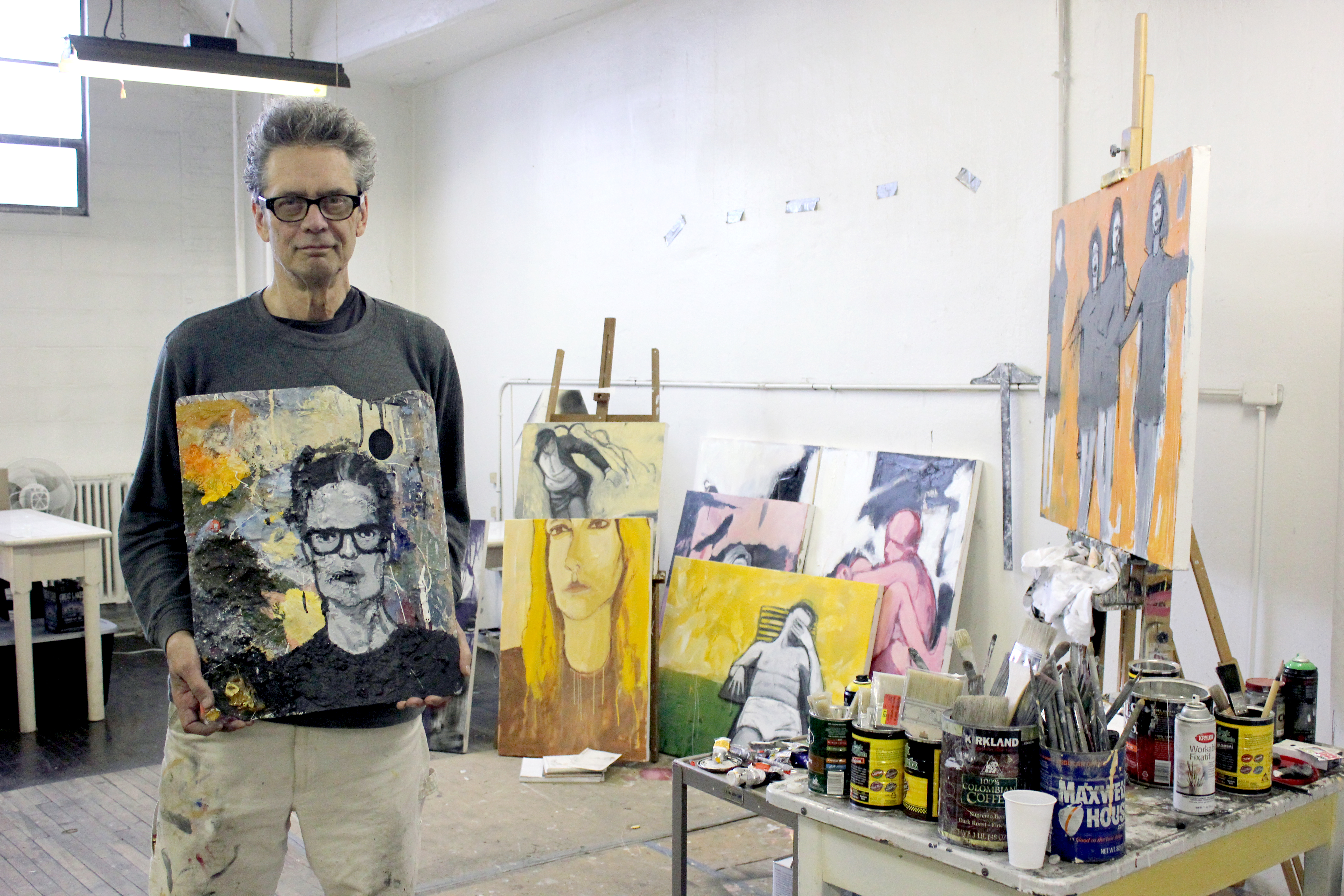 John W. Carlson holds his palette self-portrait standing inside his ArtCraft Building studio.